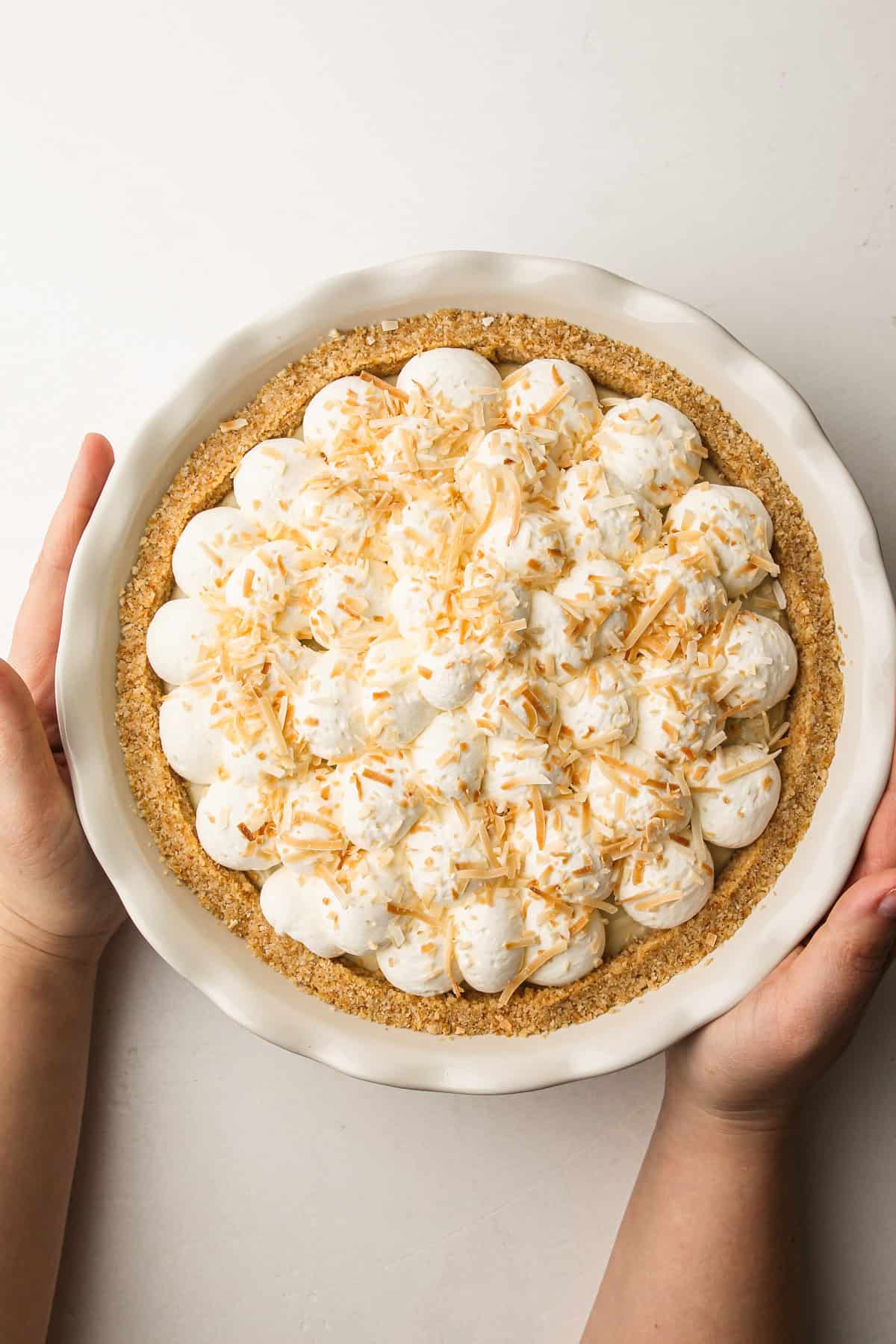 Overhead view of a coconut cream pie topped with whipped cream and toasted coconut in a ceramic pie dish.