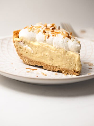 Close-up of a slice of coconut pudding pie on a plate with golden toasted coconut garnish.