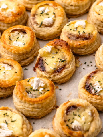 Many brie and jam puff pastry bites baked on a sheet pan with a sprinkle of rosemary.