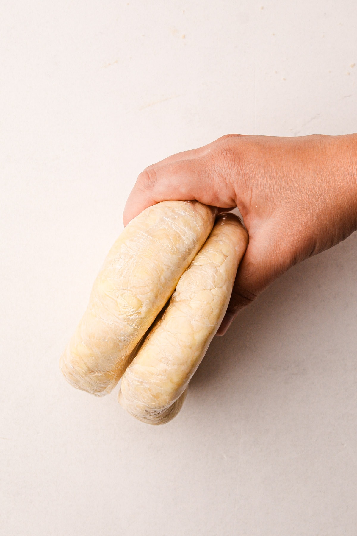 One hand holding a stack of two plastic-wrapped rounds of pie dough
