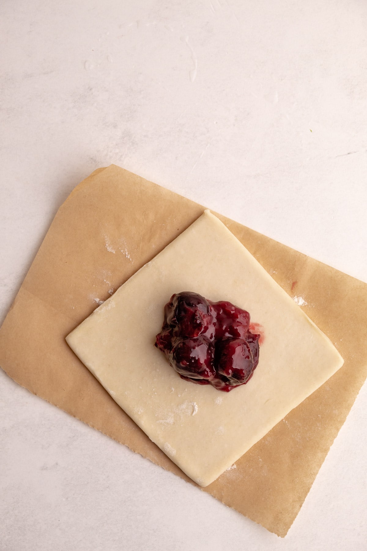 Putting cherry pie filling in puff pastry dough square.