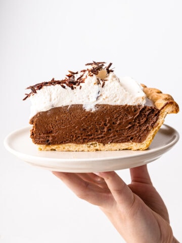 A slice of chocolate french silk pie on a plate piled high with whipped cream.