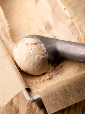 Cinnamon ice cream in a parchment-lined metal loaf tin, with a scoop formed in an ice cream scoop.