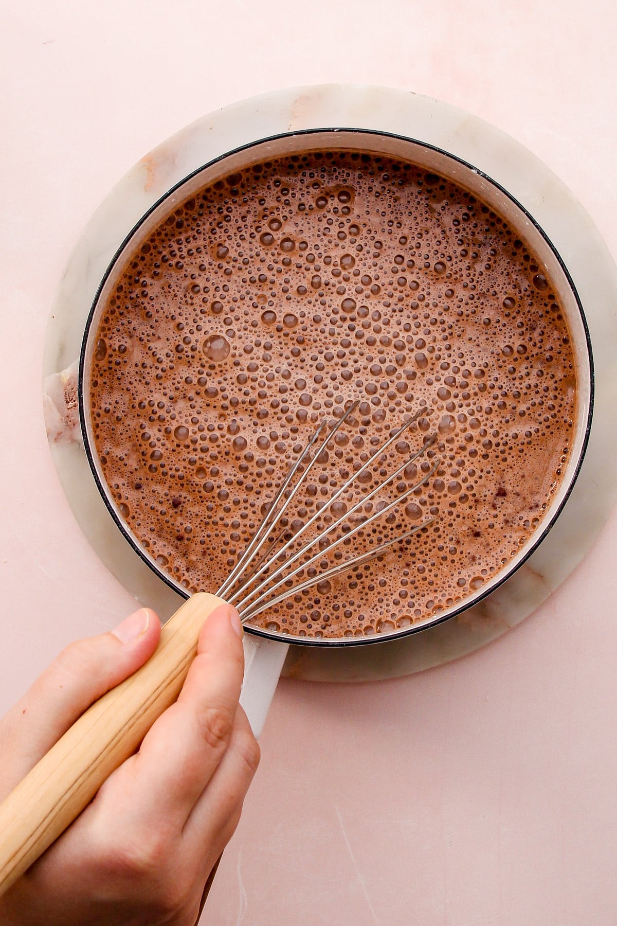 A hand whisking together ingredients for dark chocolate pudding in a saucepan.