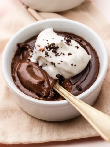 An individual serving of dark chocolate pudding in a small bowl with a spoon, topped with whipped cream and grated chocolate.