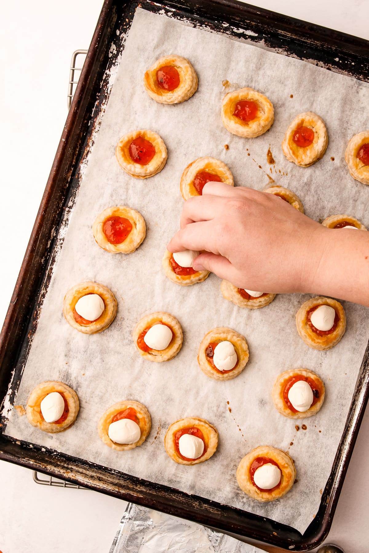 A hand placing a ball of cream cheese in the center of puff pastry rounds filled with pepper jelly for cream cheese and pepper jelly bites.