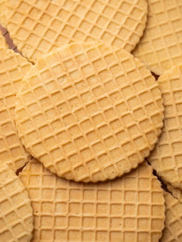 A close-up of pizzelle cookies stacked on a cooling rack, showing their crisp texture.