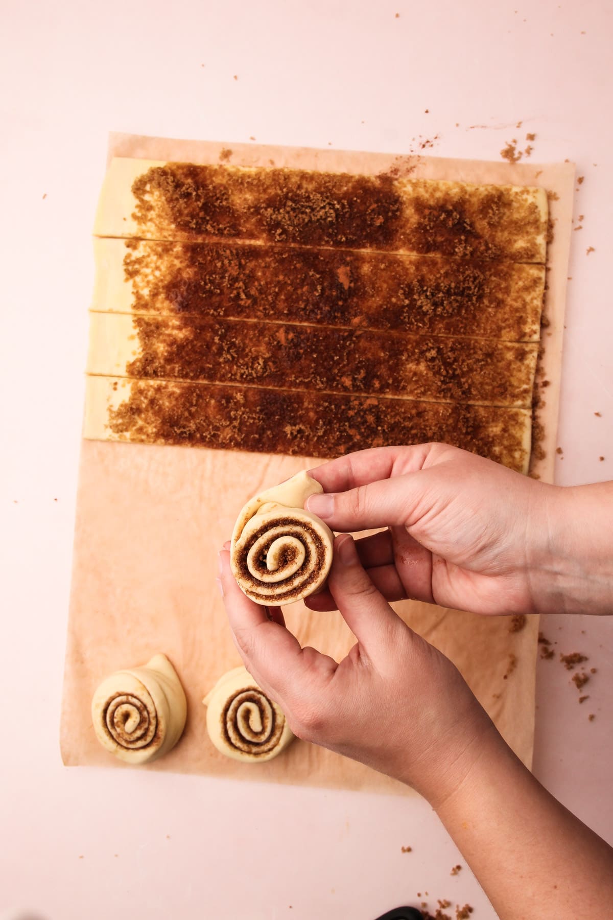 Two hands holding a shaped puff pastry cinnamon roll, tucking in the end of the pastry to the bottom.