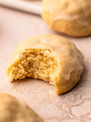 A bitten soft orange cookie with icing to reveal a moist crumb.