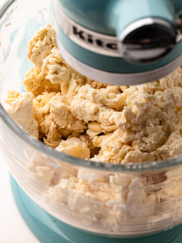 A mixture of flour and butter being mixed together in the bowl of a stand mixer