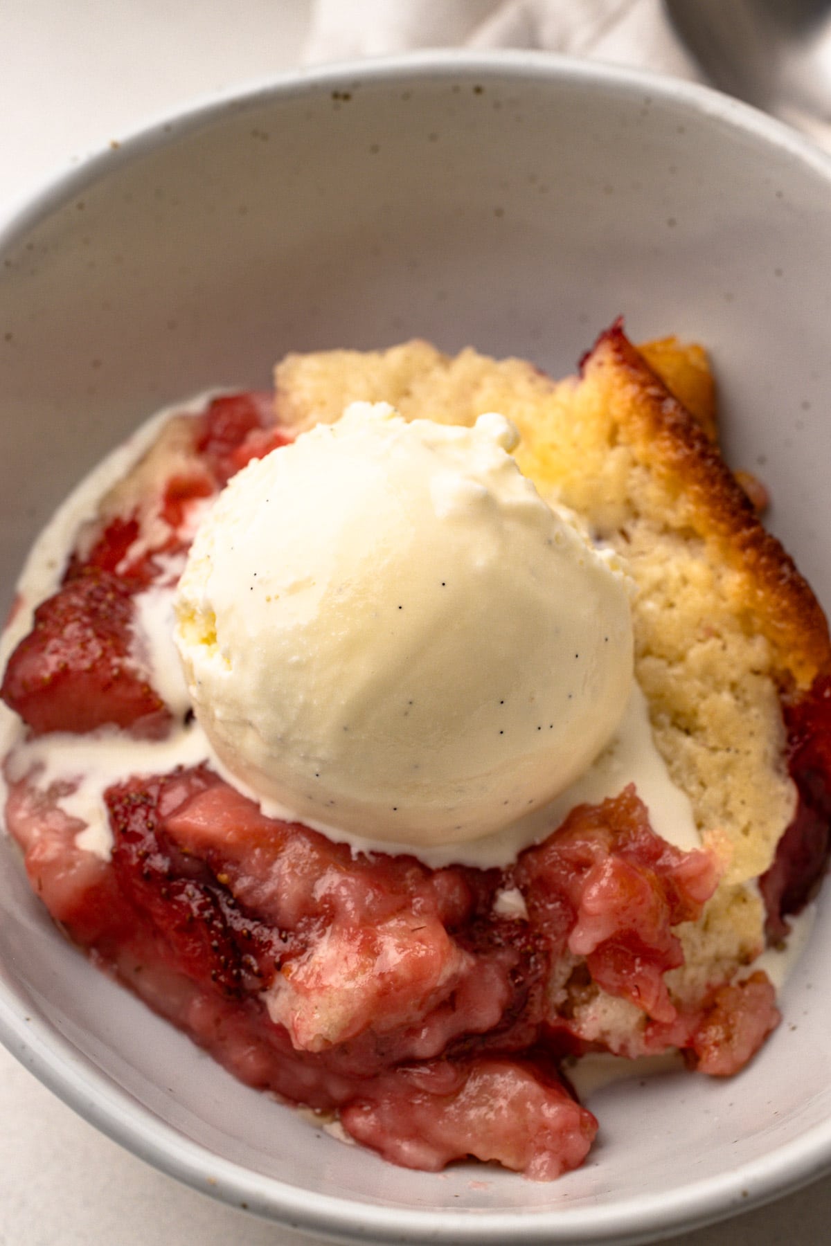 Strawberry cobbler in a bowl with a scoop of ice cream.