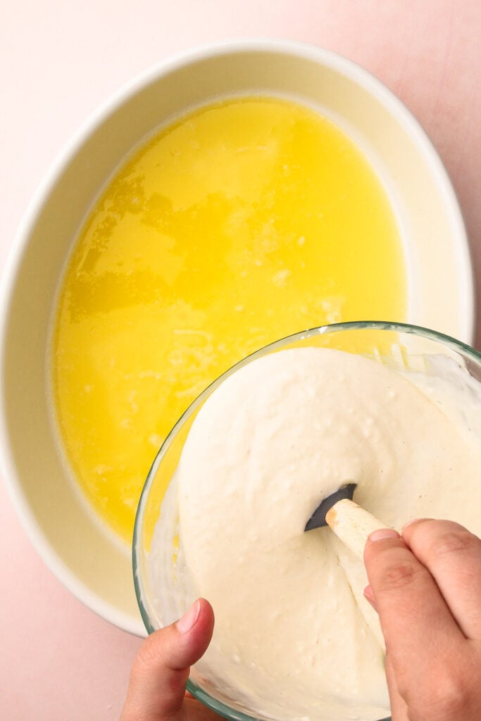 Pouring cake batter into strawberry cobbler.
